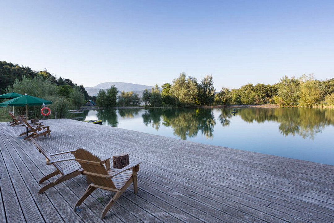 Grande terrasse en bois avec vue sur l'étang du camping Huttopia Dieulefit