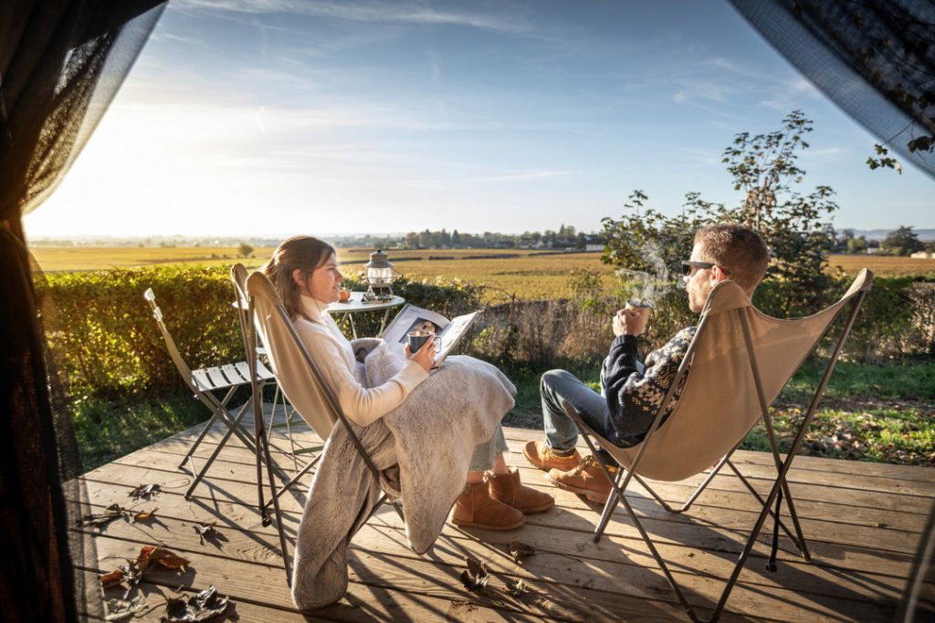Couple qui profite de la vue sur les vignes depuis la terrasse de leur hébergement au camping Huttopia Meursault